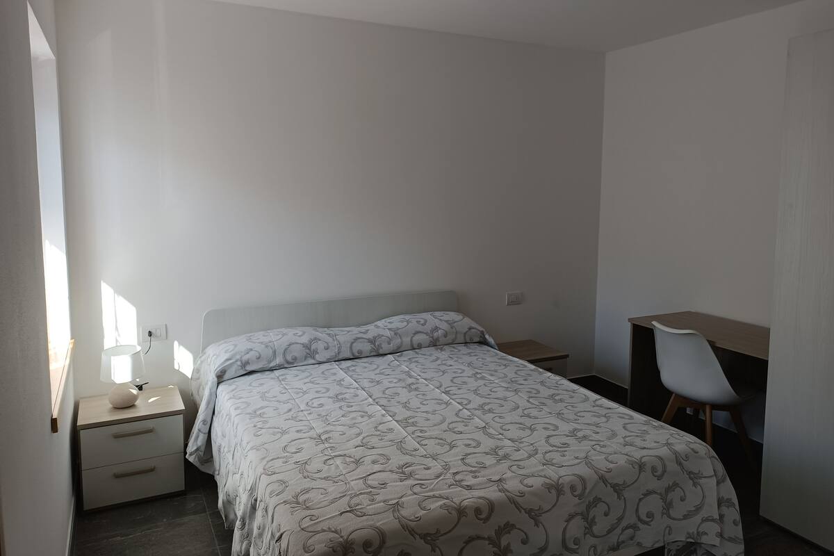 A bedroom with a bed, a nightstand, a desk, and a chair.