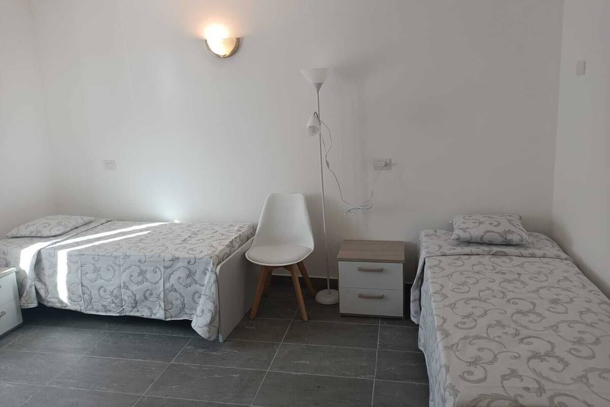 A small, clean room with two single beds, a desk, a chair, and a bedside table.