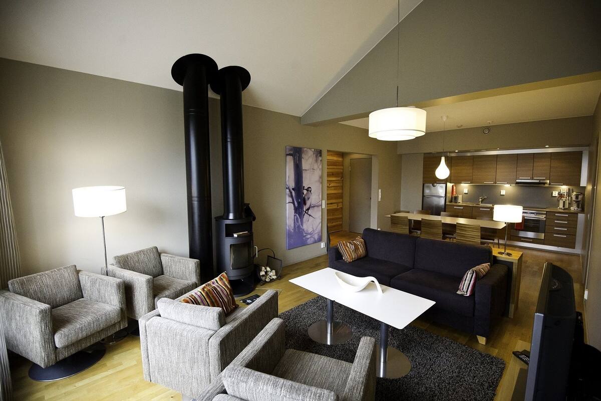 A modern living room with a fireplace, sofas, a coffee table, and a kitchen area.