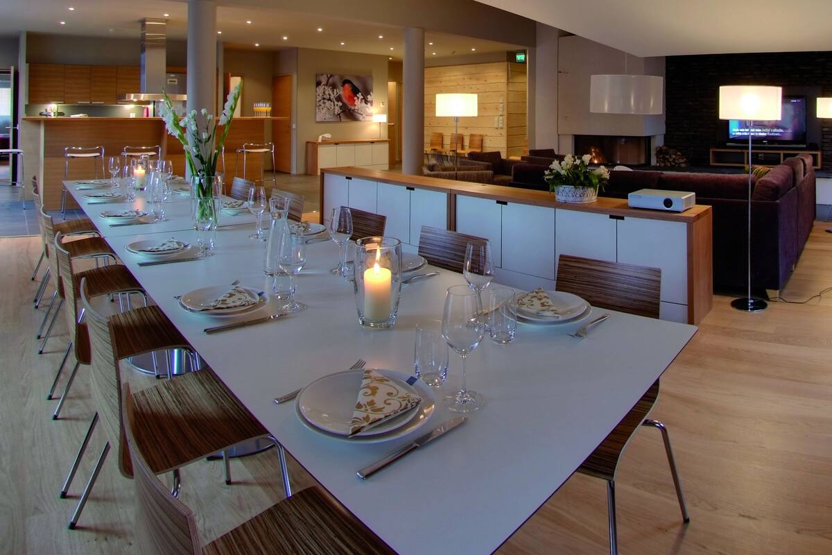 A long dining table set with plates, glasses, and candles, flanked by wooden chairs.