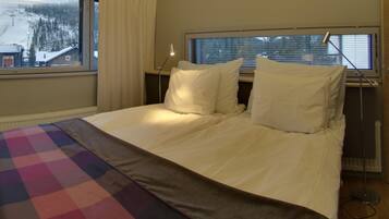 A hotel room with a bed, a window with blinds, a lamp, and a view of a snowy landscape.