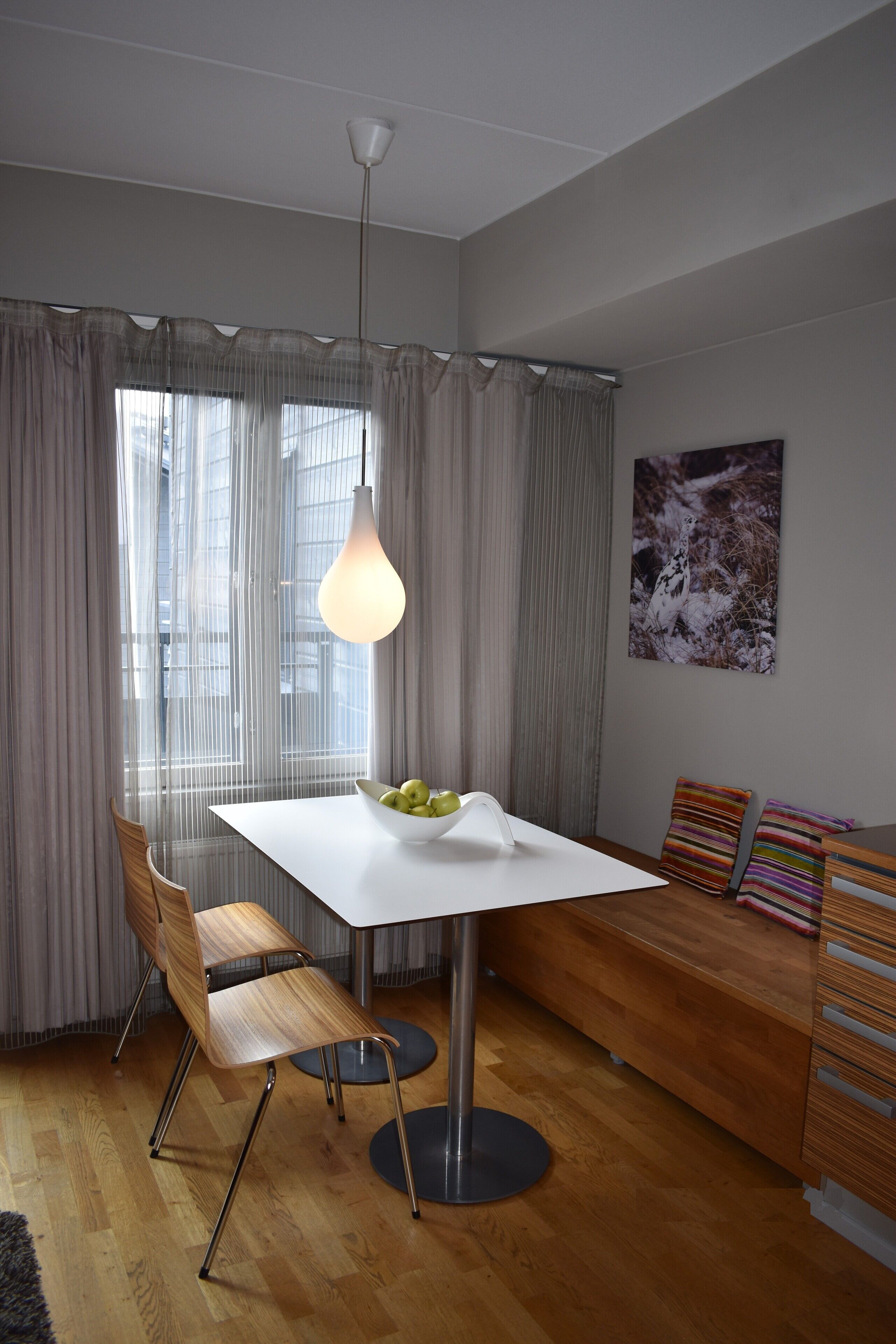 Et moderne spiseområde med et hvidt bord, en skål med frugt og en hængende lampe.