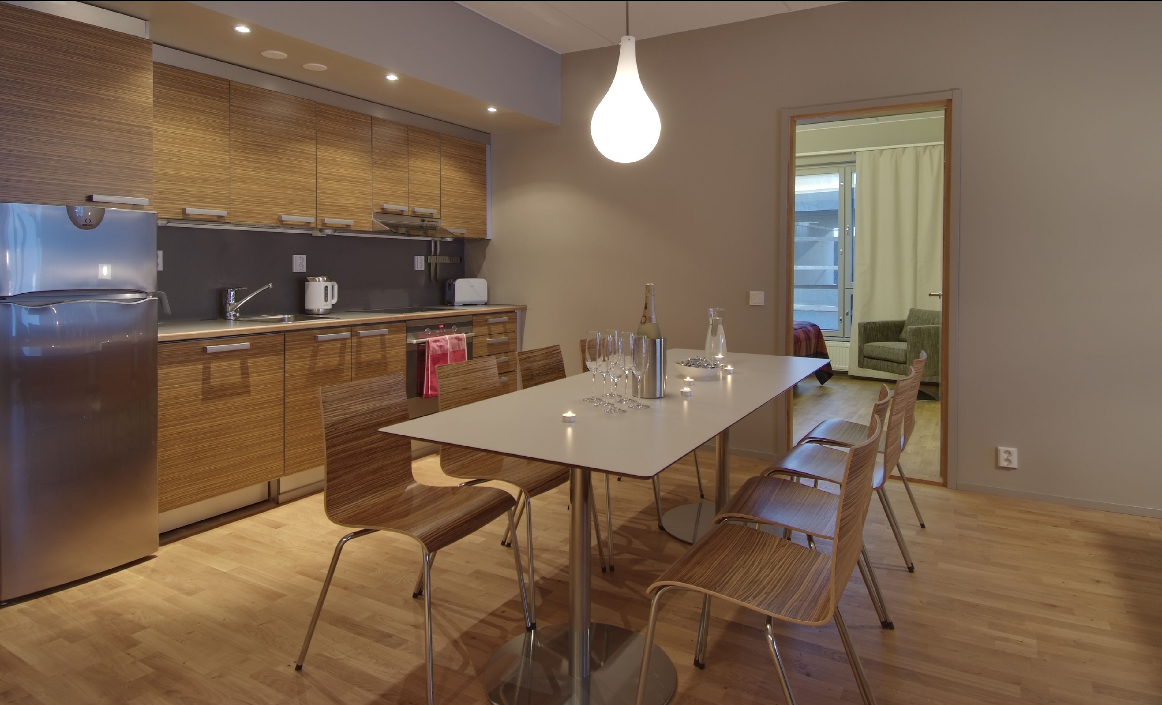 Una cucina moderna con mobili in legno, un frigorifero in acciaio inossidabile e un'area pranzo con tavolo bianco e sedie in metallo.