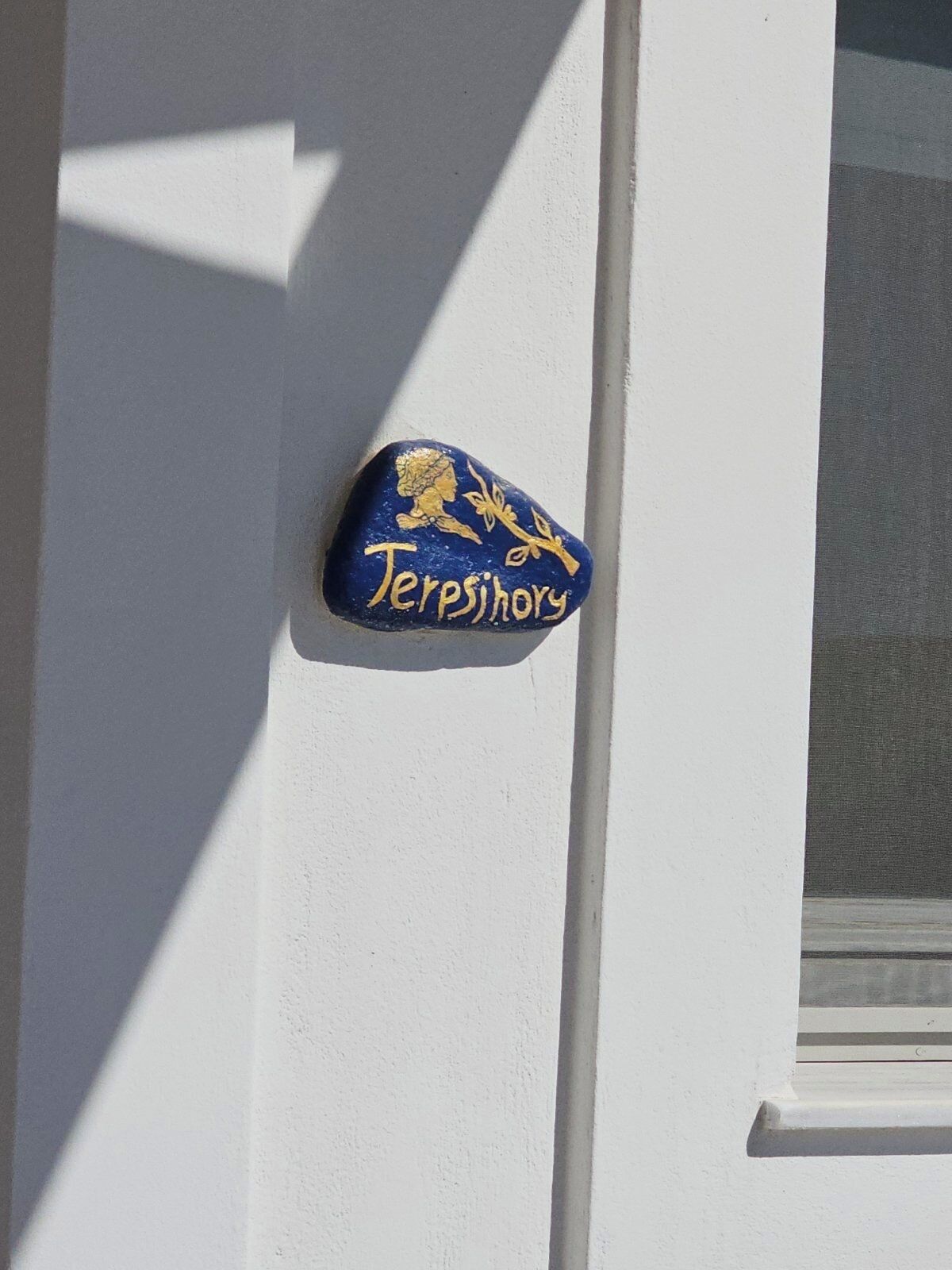 A blue plaque with gold lettering on a white wall, reading "Terpsihory".