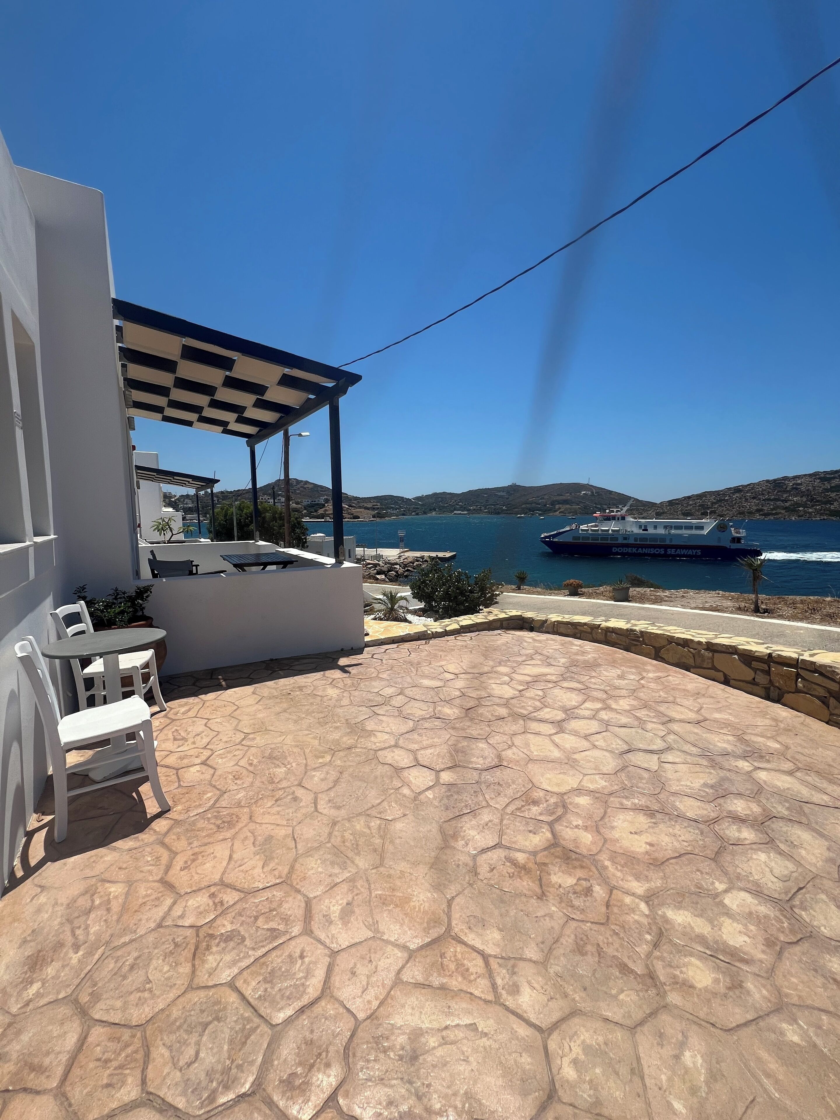 A patio with hexagonal stone flooring, white outdoor furniture, and a view of the sea and hills.