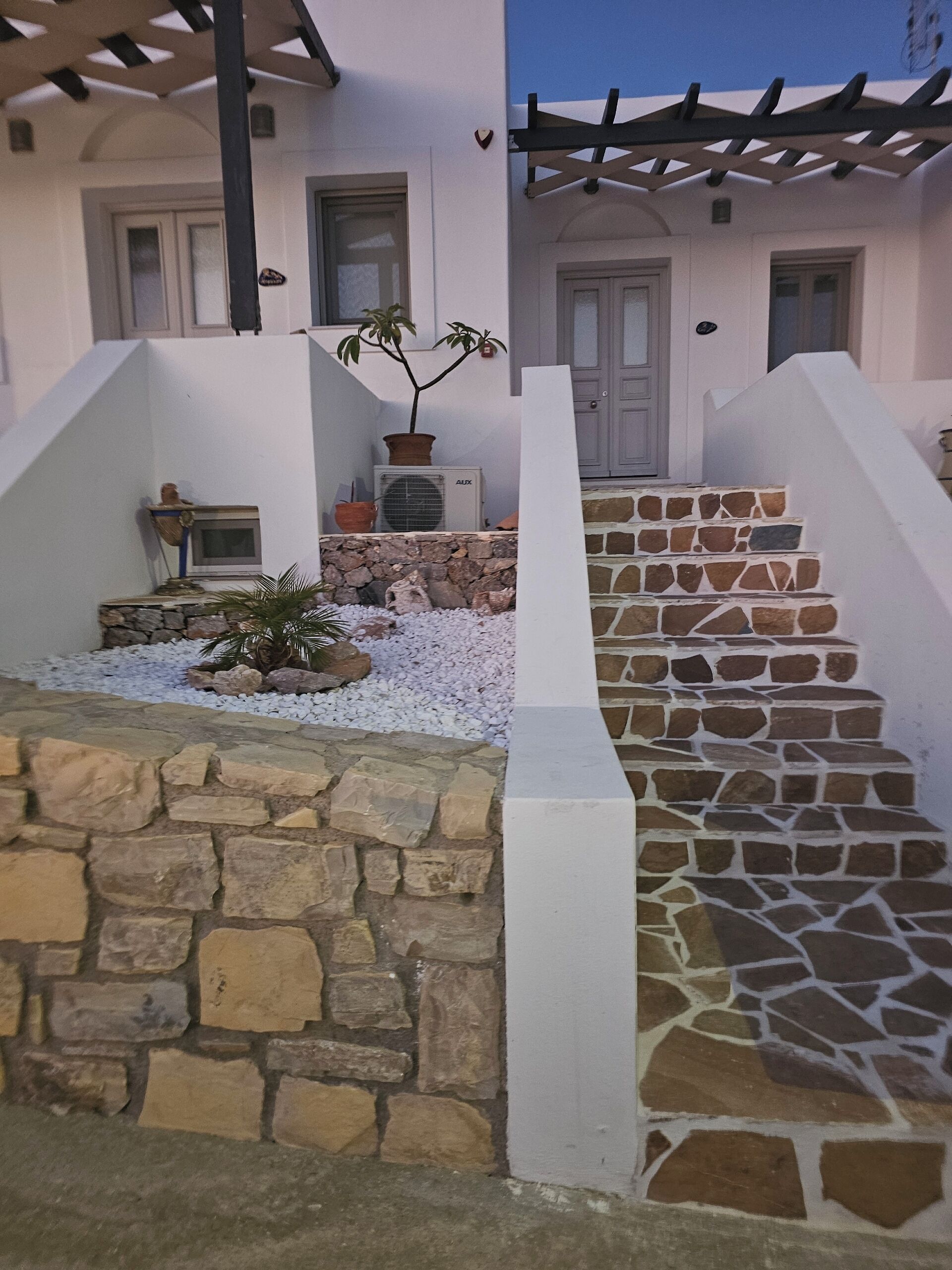 Eine Steintreppe führt zu einer weißen Tür, einem Blumentopf und einer kleinen Statue auf der linken Seite.