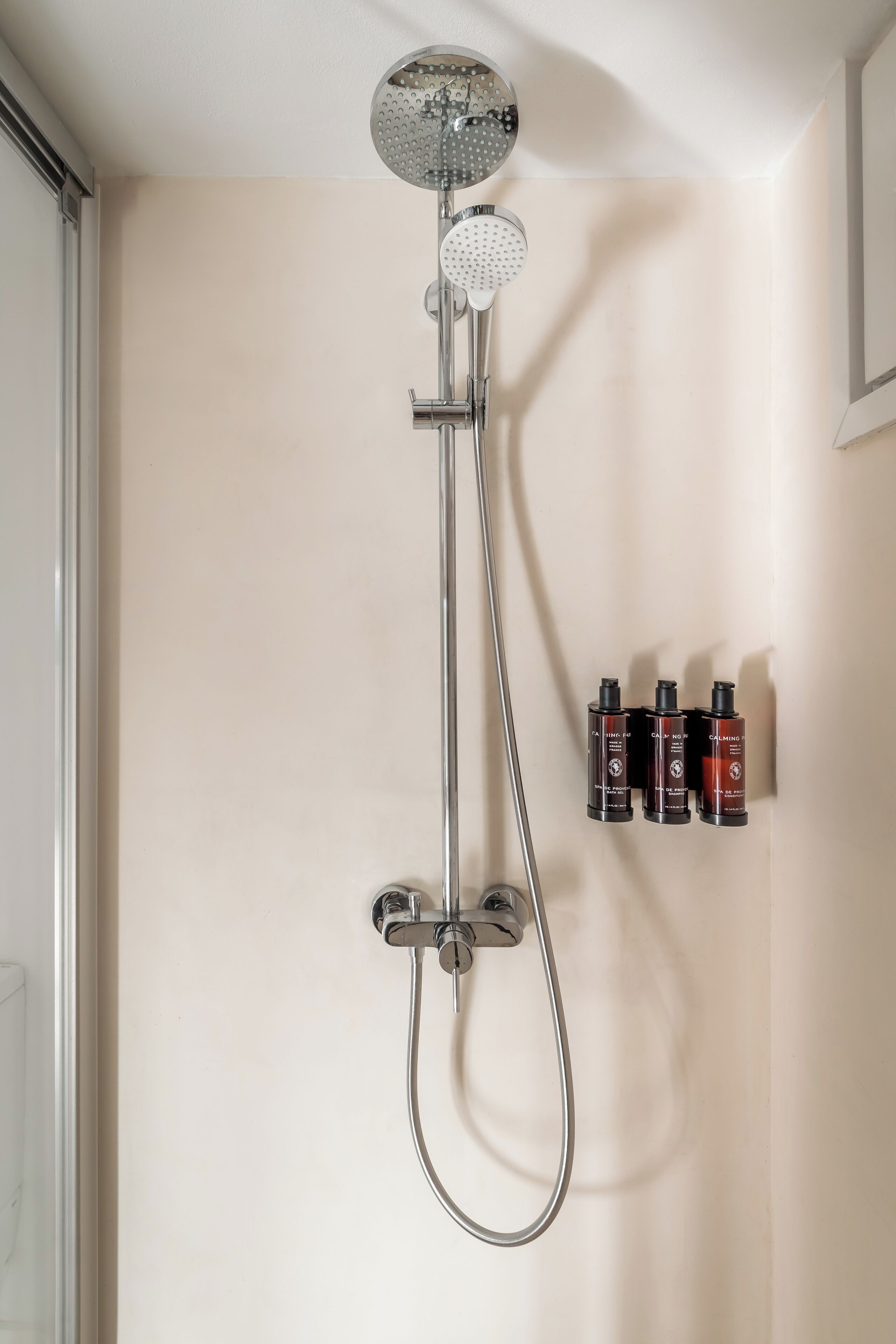 A shower with a handheld showerhead and a wall-mounted control panel.