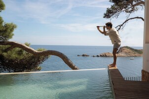 Un hombre tomando una foto en una terraza de madera con vista a un mar azul y despejado, con una isla rocosa en la distancia.
