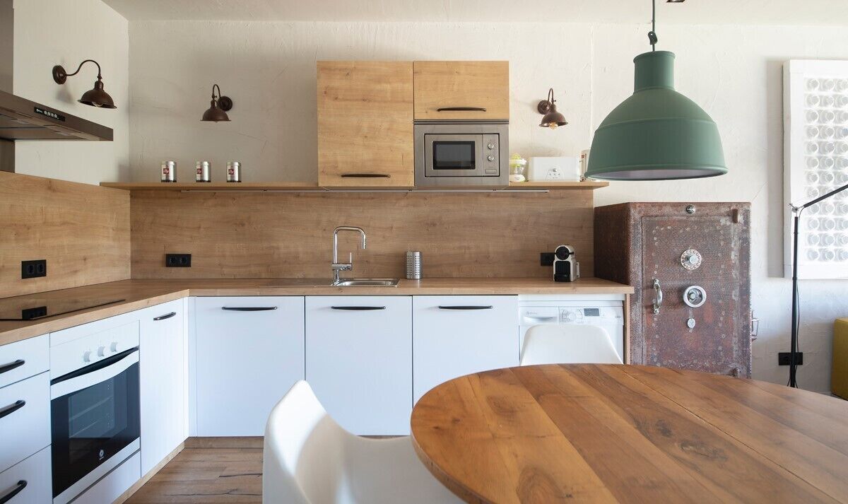 Une cuisine moderne avec des meubles en bois, un four encastré, un four à micro-ondes et un luminaire suspendu vert.