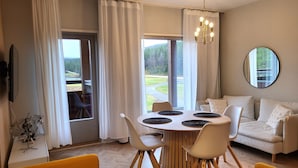 Un salón moderno con una mesa de comedor redonda, sofás blancos y un amplio ventanal con vistas a una zona boscosa.