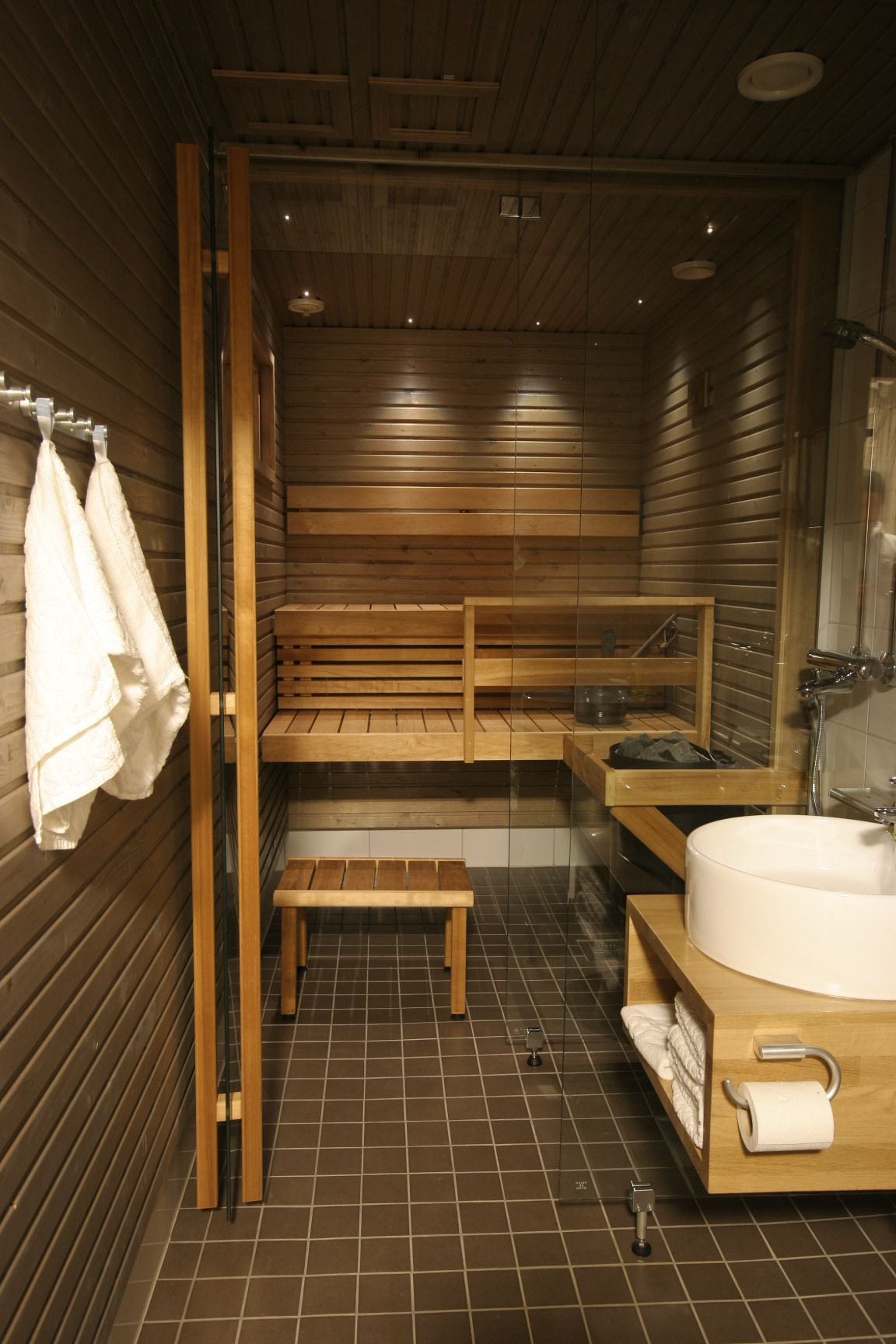 A sauna room with wooden benches, a sink, and towels.