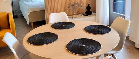 A modern room with a round table, four chairs, a bed, a TV, and a window with curtains.