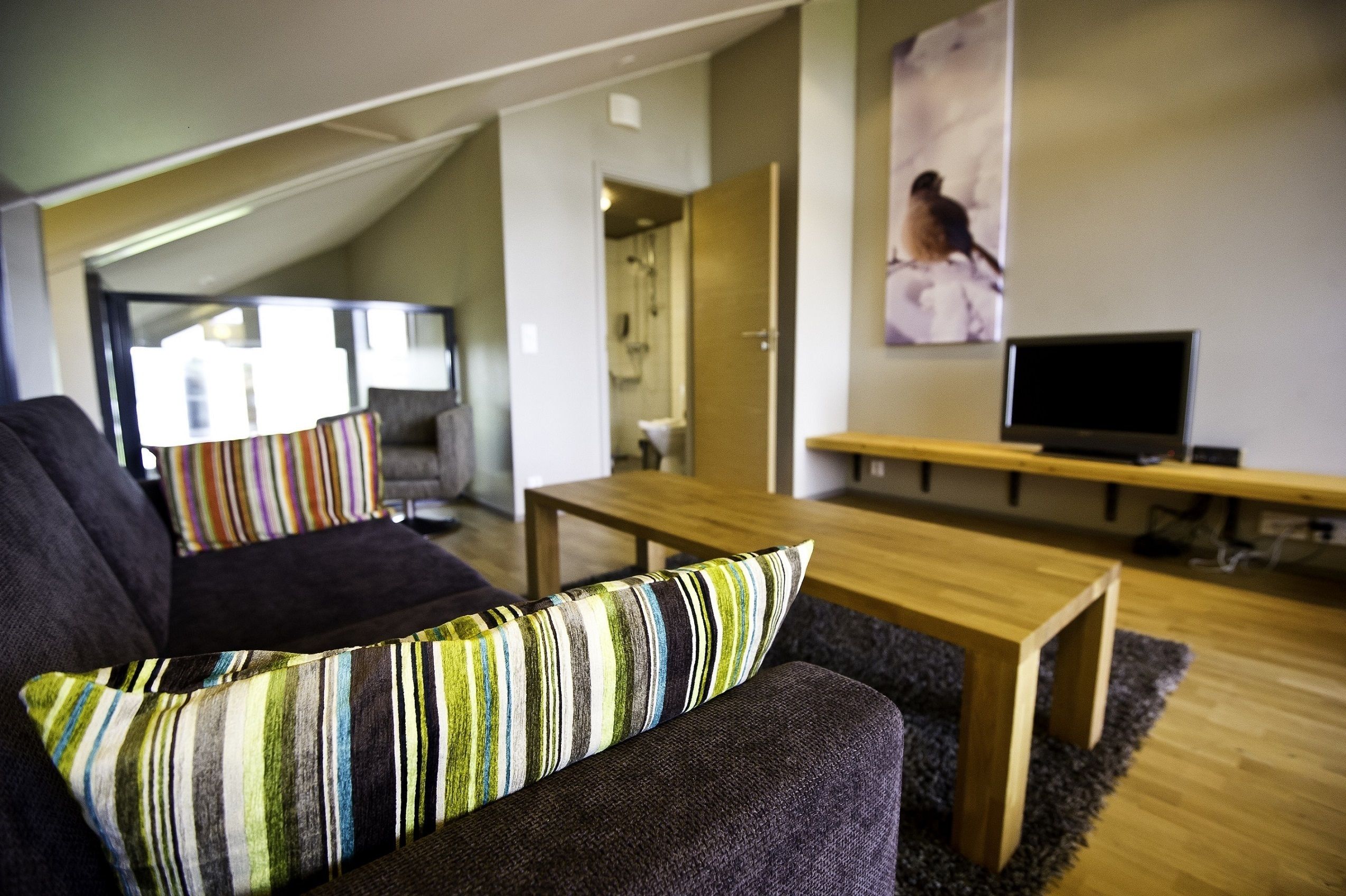 Un salon moderne avec un canapé foncé, des coussins à rayures, une table basse en bois et un téléviseur à écran plat.