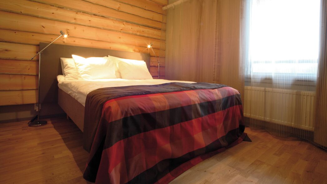 A wooden-paneled room with a bed, a floor lamp, and a window with curtains.