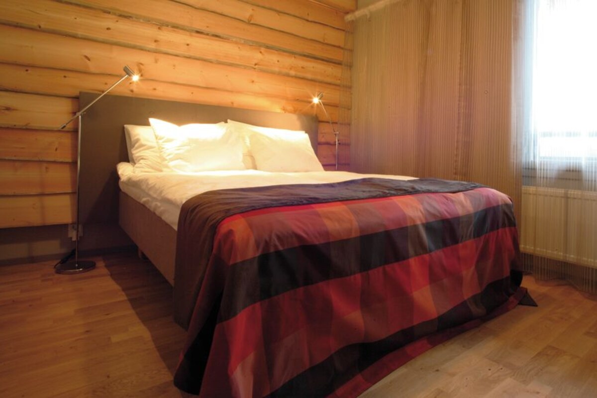 Ein Zimmer mit Holzwandverkleidung, einem Bett, einer Stehlampe und einem fenster mit Vorhängen.