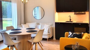 Una sala de estar moderna con comedor, cocina y un ventanal con vistas a un bosque.