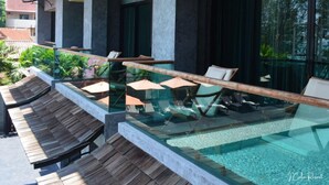 A modern outdoor pool area with glass barriers, lounge chairs, and a wooden deck. - I Calm Resort (Cha-am)