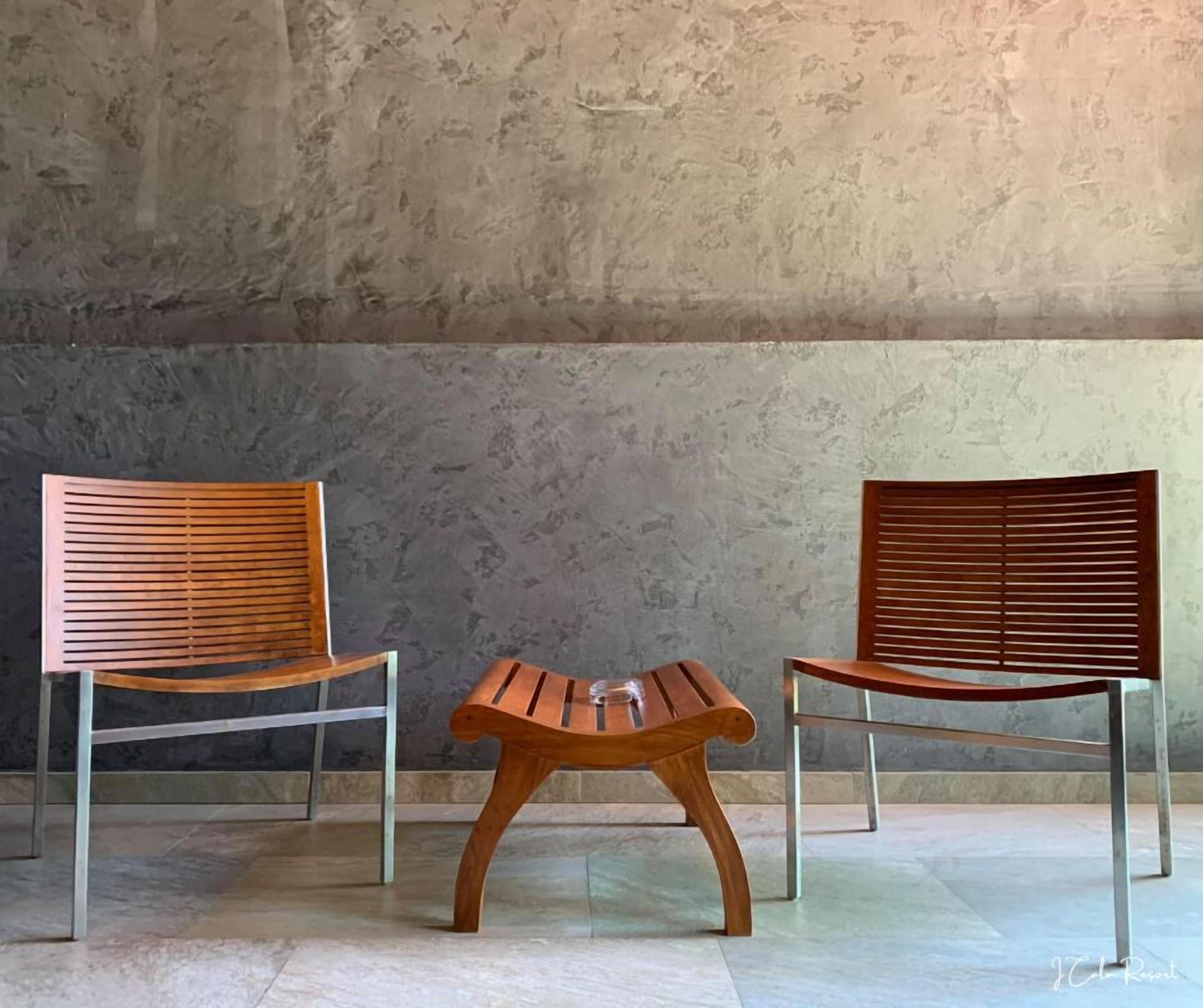 Two wooden chairs with metal frames and a small wooden table in a room with a textured wall and tiled floor.