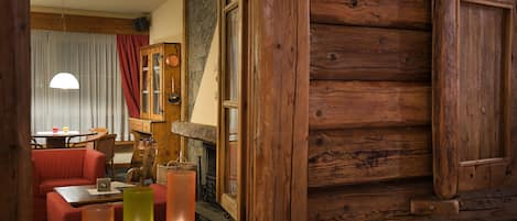 A cozy cabin interior with a wooden log wall, a dining area with a table and chairs, and a red sofa.