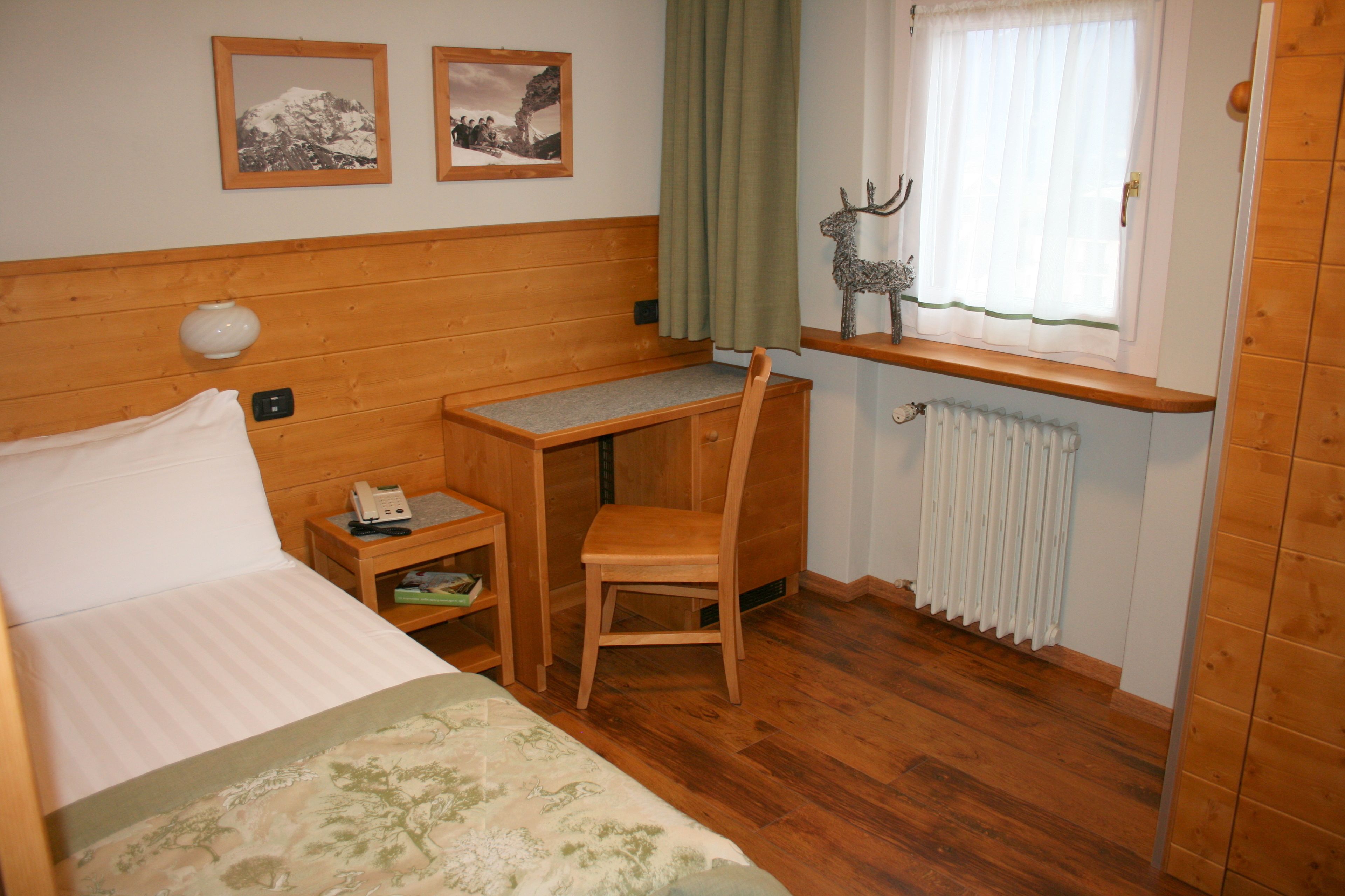 Una habitación con cama, escritorio, silla, radiador y dos cuadros en la pared.