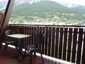 A balcony with a table and two chairs, overlooking a mountainous landscape with a village below. - Hotel Larice Bianco (Bormio)