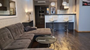 A modern living room with a sofa, a glass coffee table, and a kitchen area with a bar and two bar stools. - Willa Klodzko - Zacisze (Klodzko Miasto)