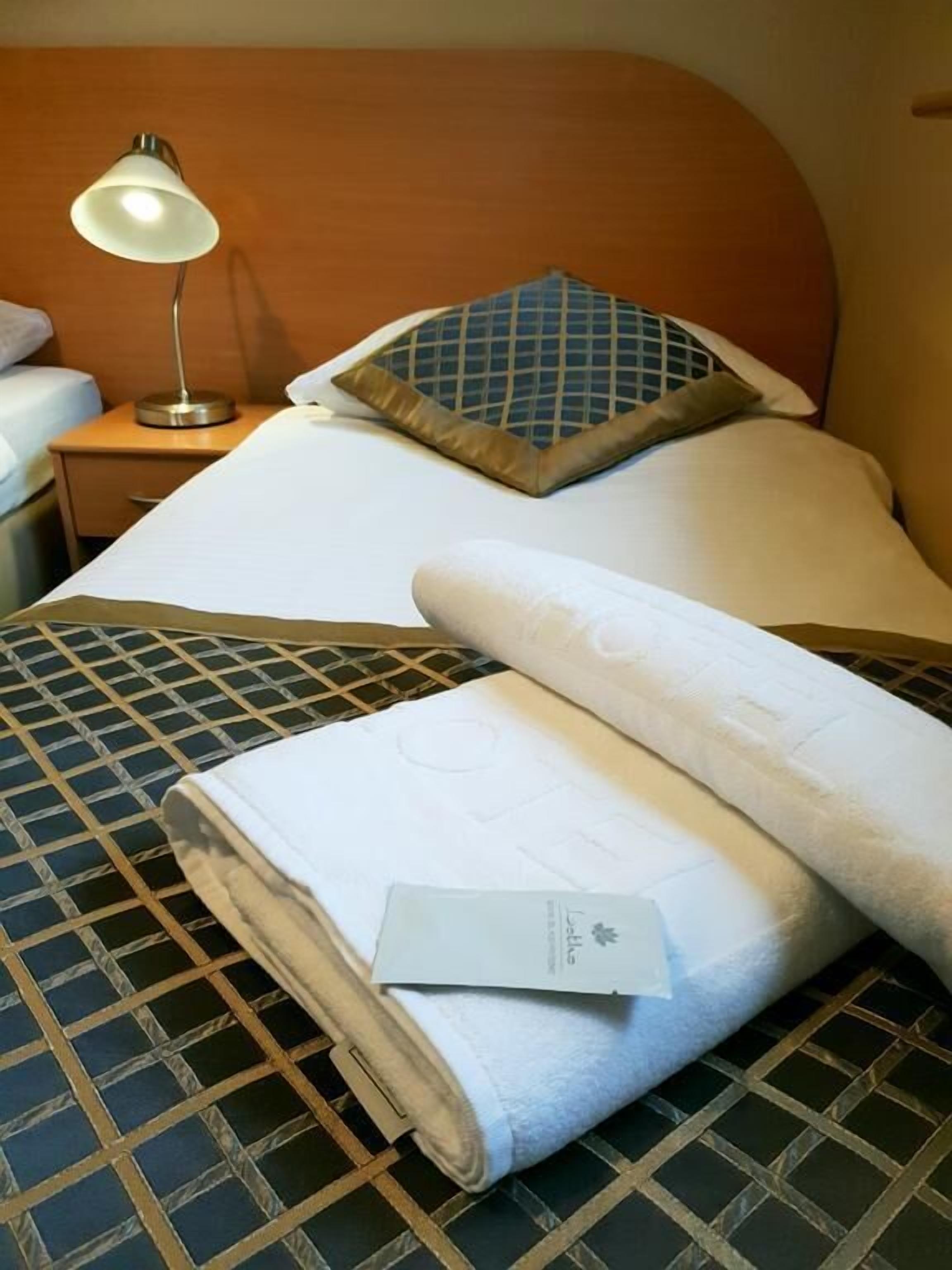 A neatly made bed with a patterned bedspread, a pillow with a geometric design, and a bedside lamp on a wooden nightstand.