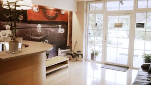 A reception area with a wooden counter, a large window with a view of the outside, and a sign on the door. - Willa Klodzko - Zacisze (Klodzko Miasto)