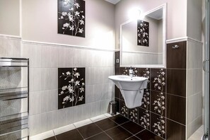 Une salle de bain avec un lavabo blanc, des carreaux de couleur marron foncé et des motifs floraux décoratifs sur les murs.