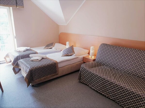 Une chambre d’hôtel avec deux lits simples, un canapé, une table de chevet avec une lampe et une fenêtre donnant sur un paysage agréable.