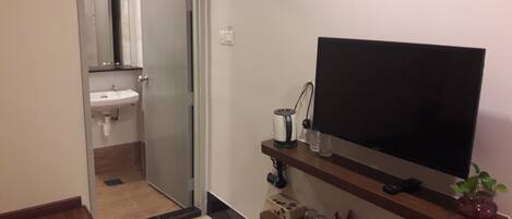 A hotel room with a TV on a wooden shelf, a sink, and a door leading to another room.
