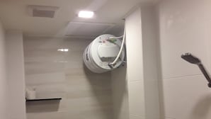 A small, tiled bathroom with a toilet, a shower, and a wall-mounted water heater. - De Benz Inn (Malacca City)