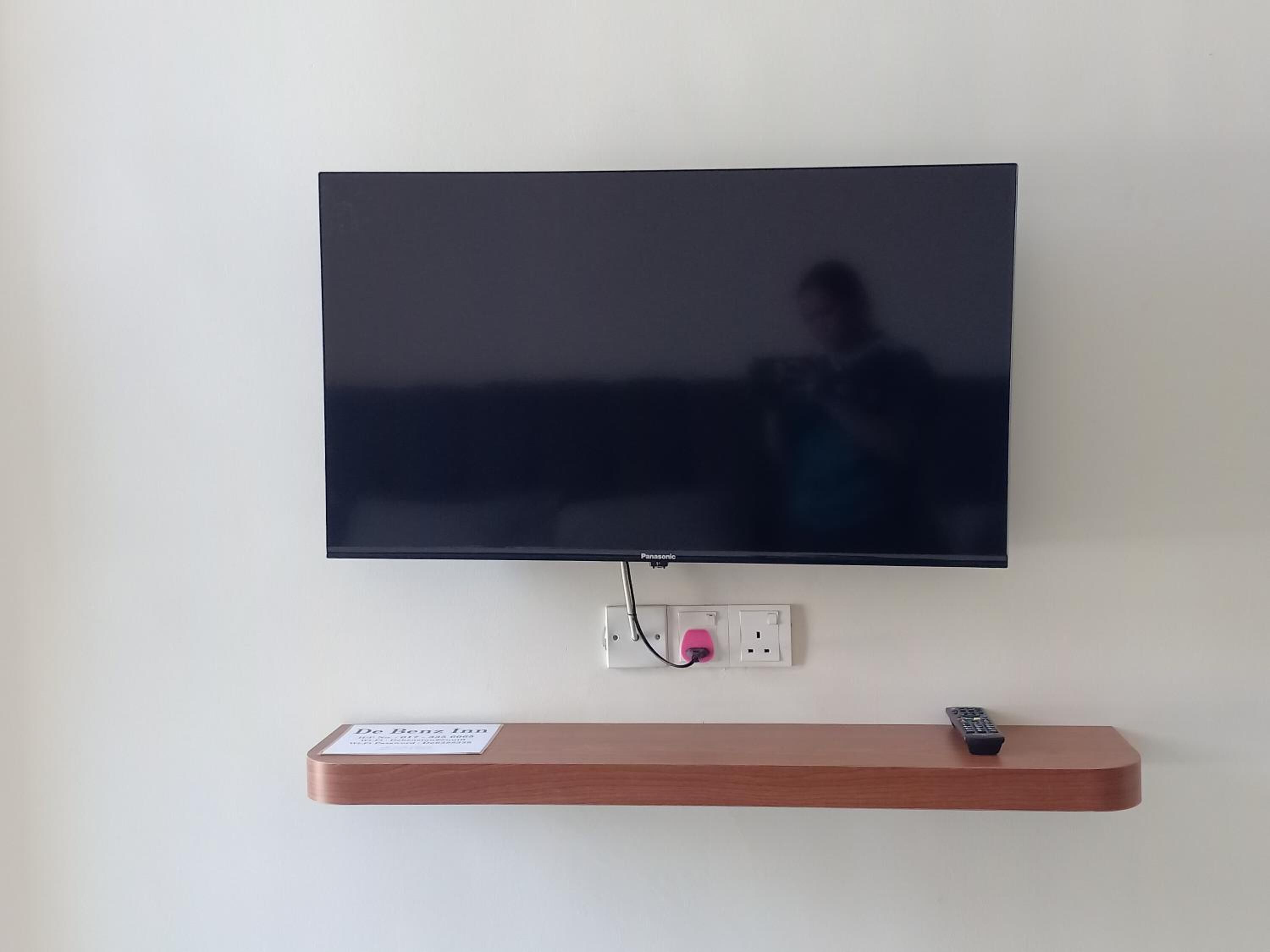 Un téléviseur à écran plat fixé au mur, avec une étagère en bois placée en dessous.