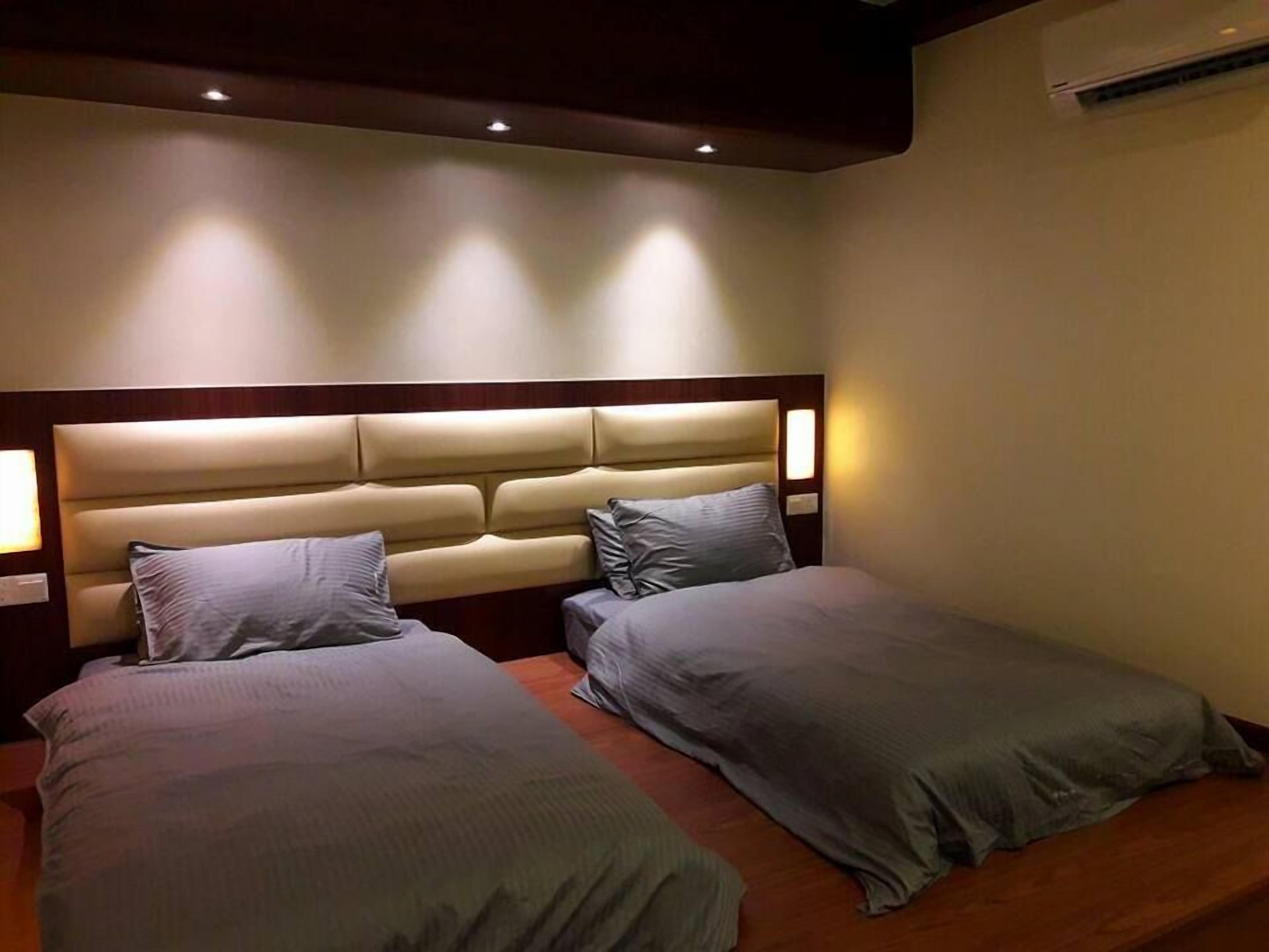 Quarto de hotel com duas camas de solteiro, cabeceira de madeira e luminárias de cabeceira.