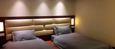 Quarto de hotel com duas camas de solteiro, cabeceira de madeira e luminárias de cabeceira.