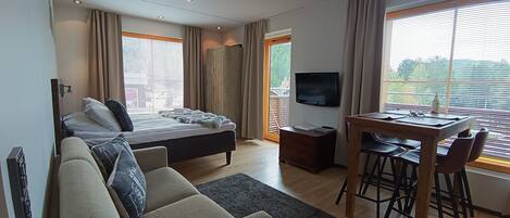 Une chambre d’hôtel comprenant un lit, un canapé, une table à manger avec des chaises, une télévision et de grandes fenêtres avec des rideaux.