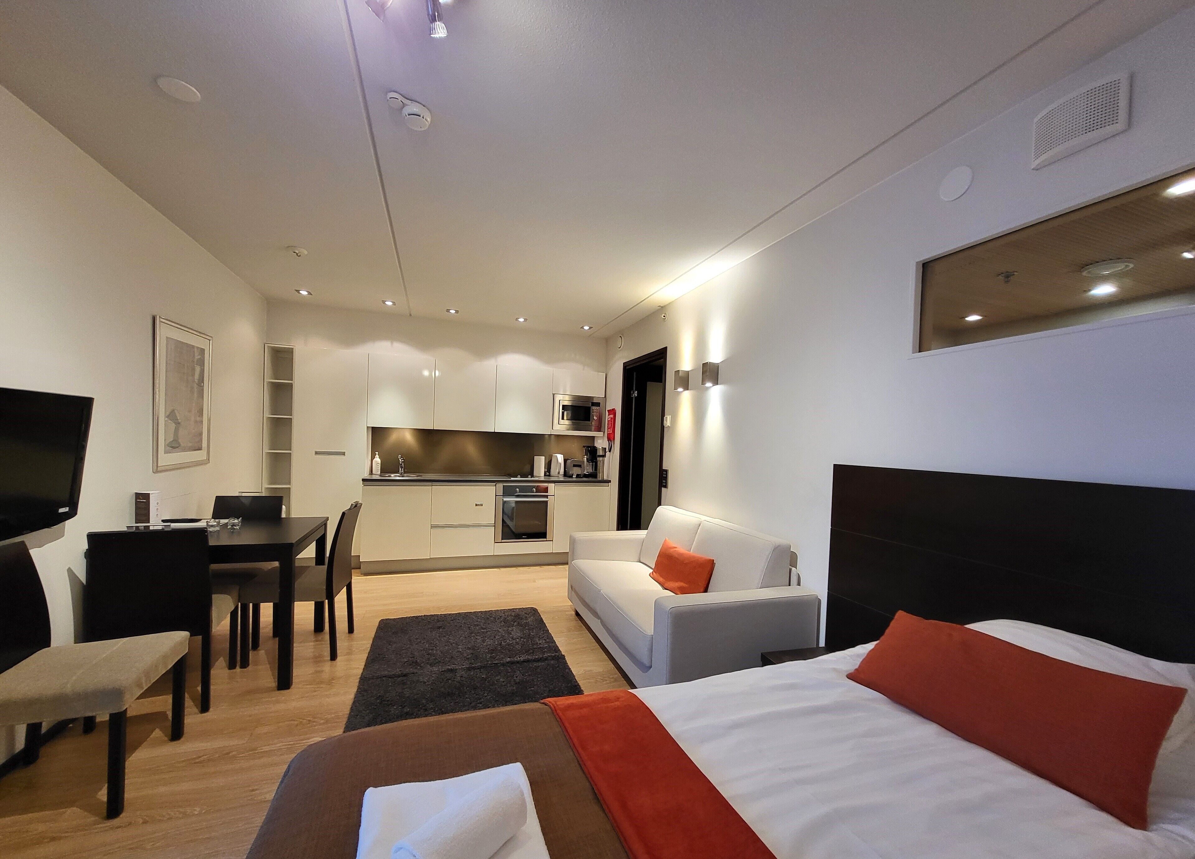 Ein modernes Hotelzimmer mit einem Bett, einer Couch, einem Schreibtisch und einer Küchenzeile.