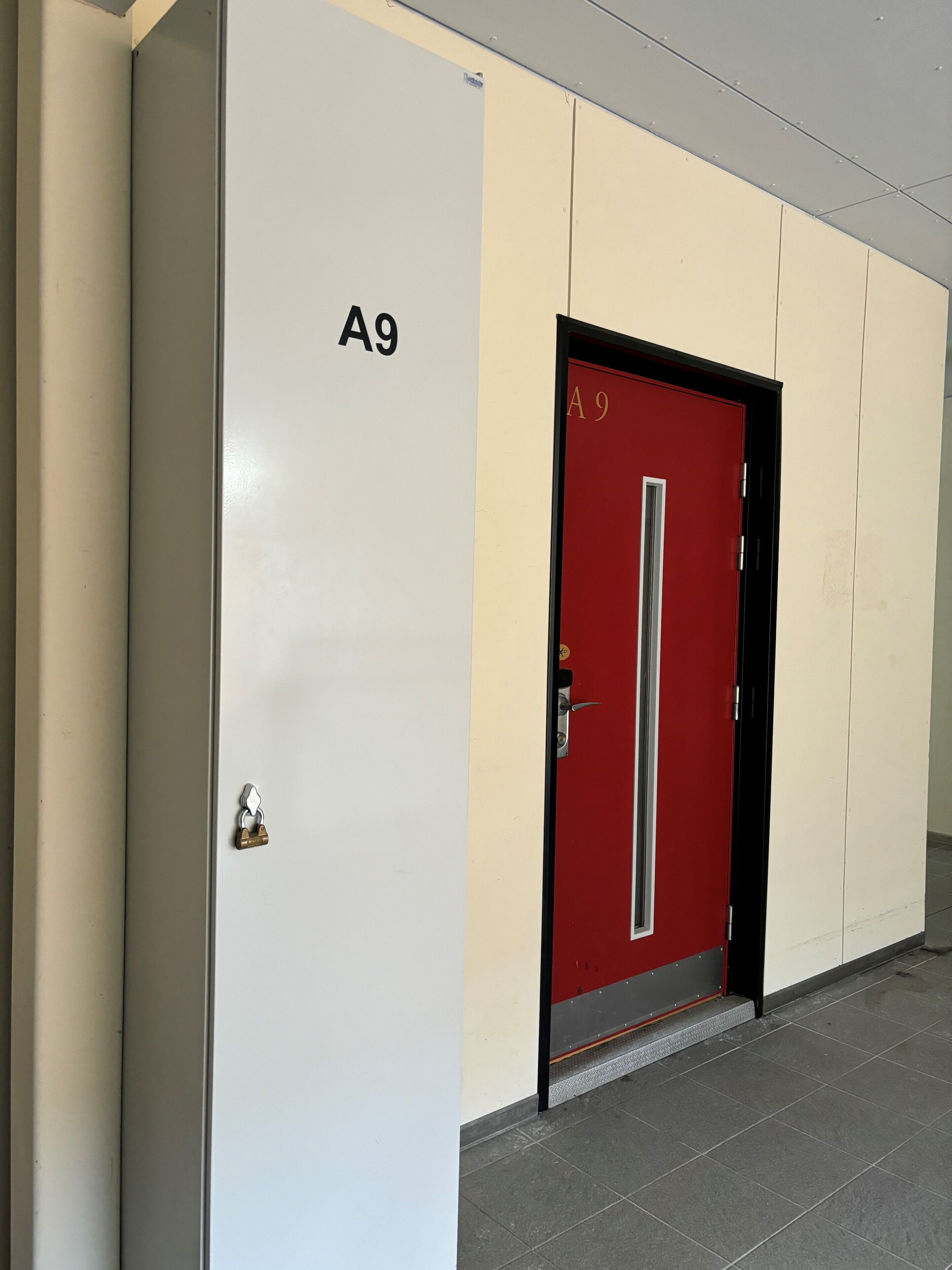 A hallway with a white wall and a red door labeled A9.