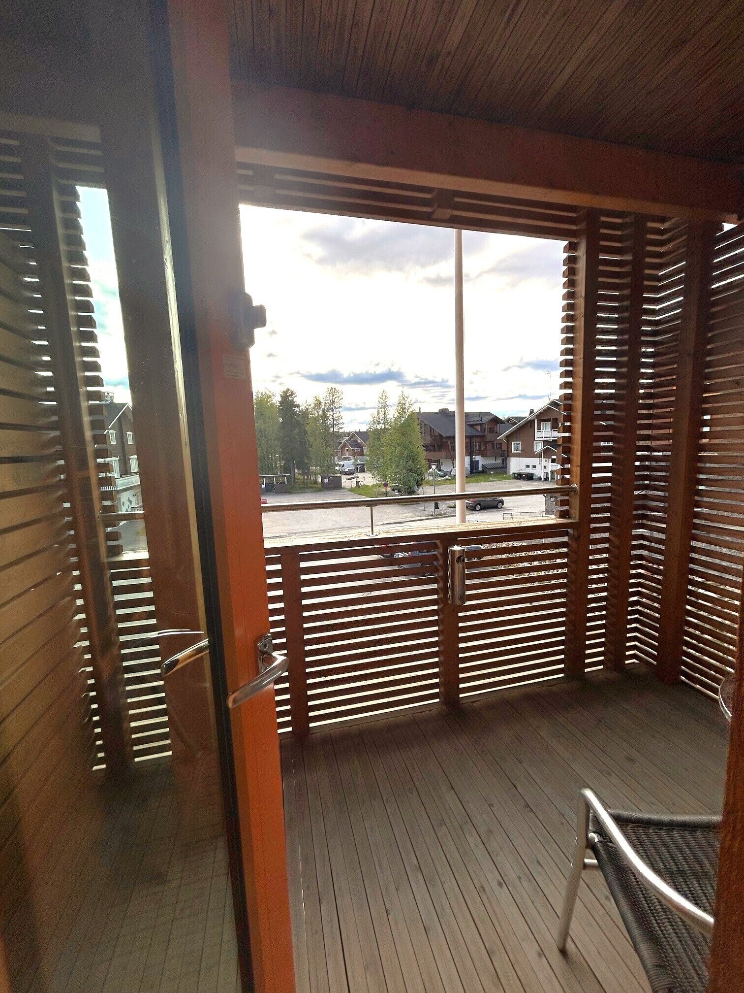 A wooden deck with a metal railing, a view of a residential area, and a clear sky.