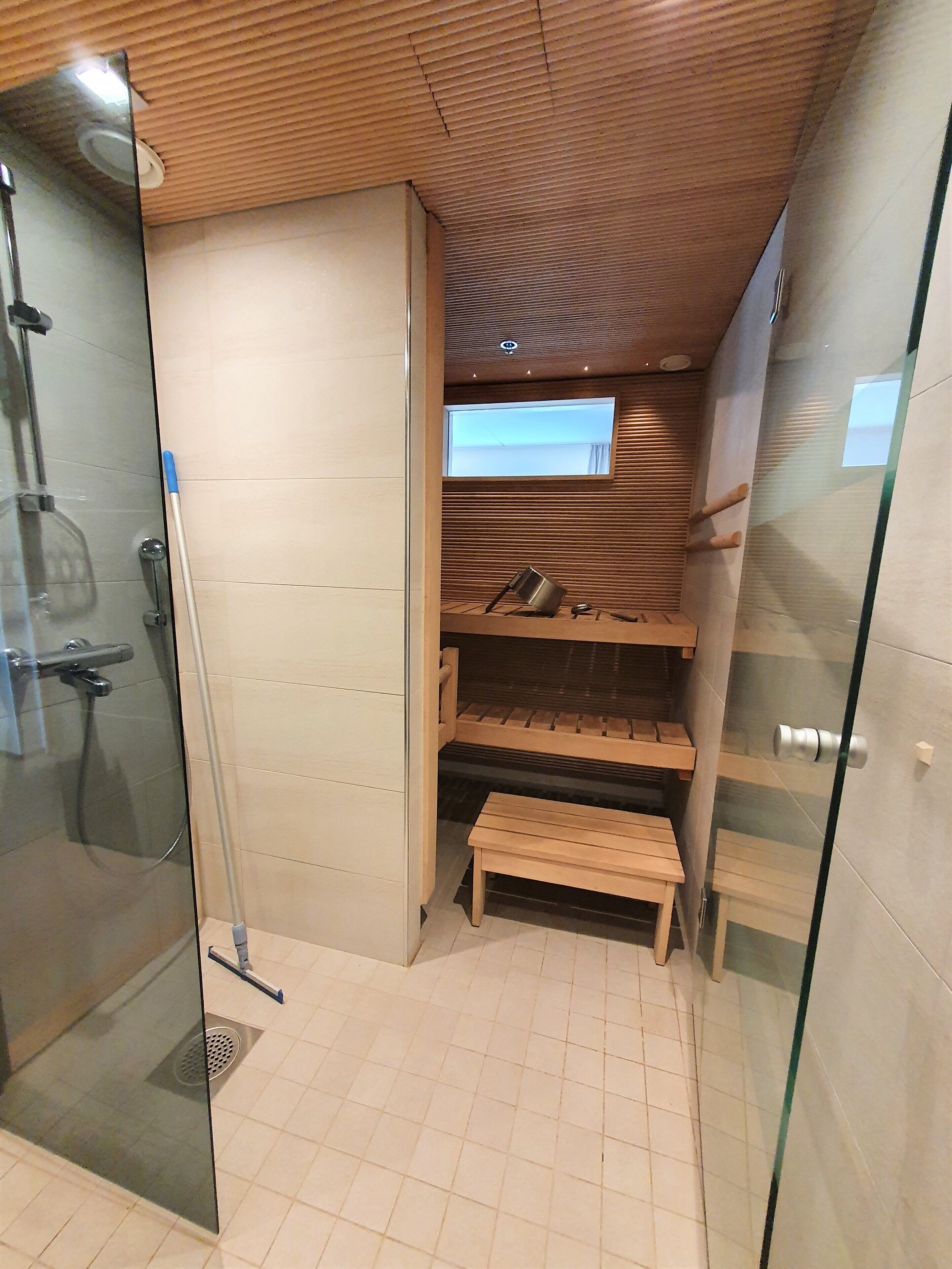 A modern bathroom with a glass shower enclosure, wooden shelves, and a bench.