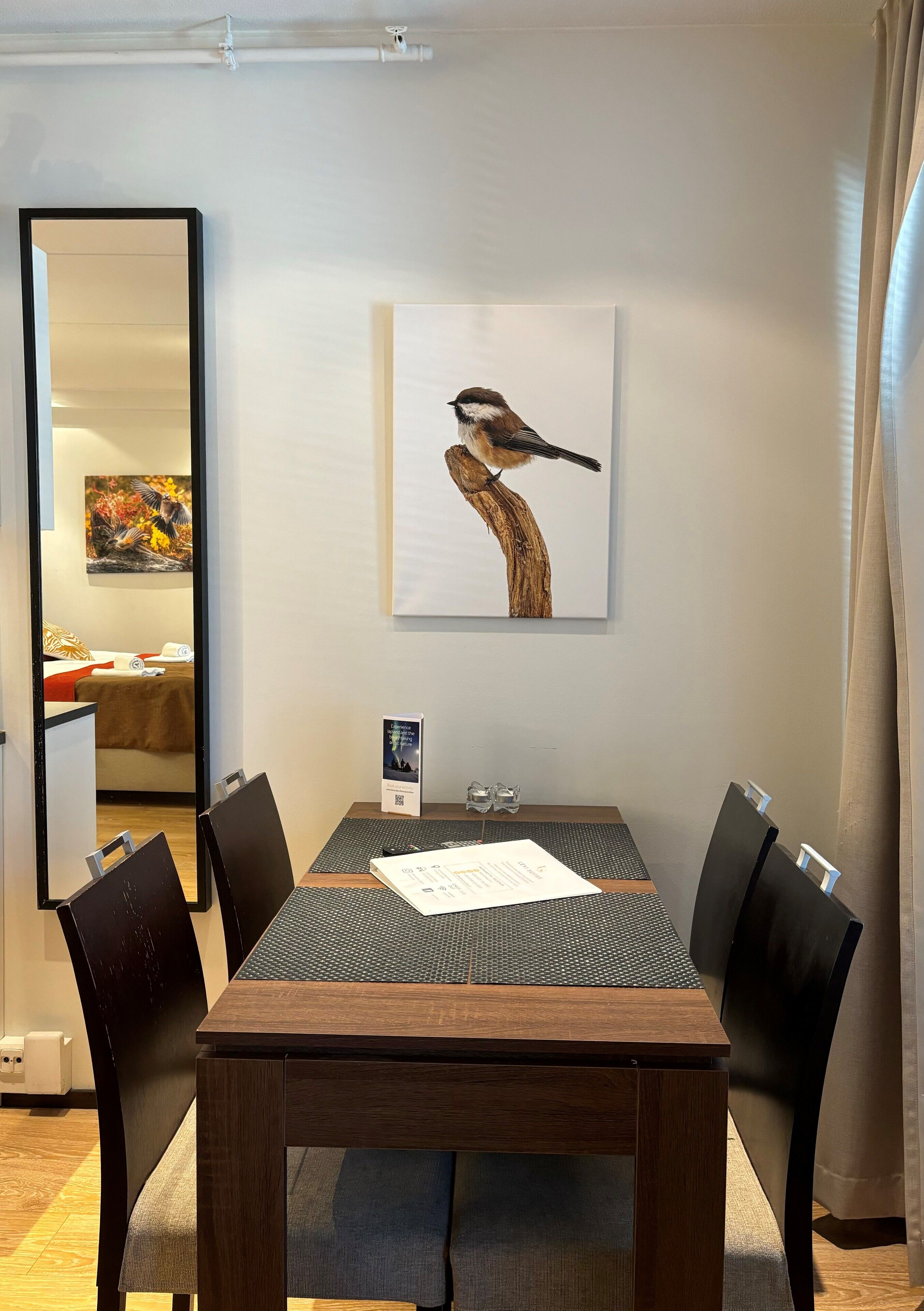 Ein Essbereich mit einem Holztisch, schwarzen Stühlen, einem großen Spiegel und einem Wandbild eines Vogels.