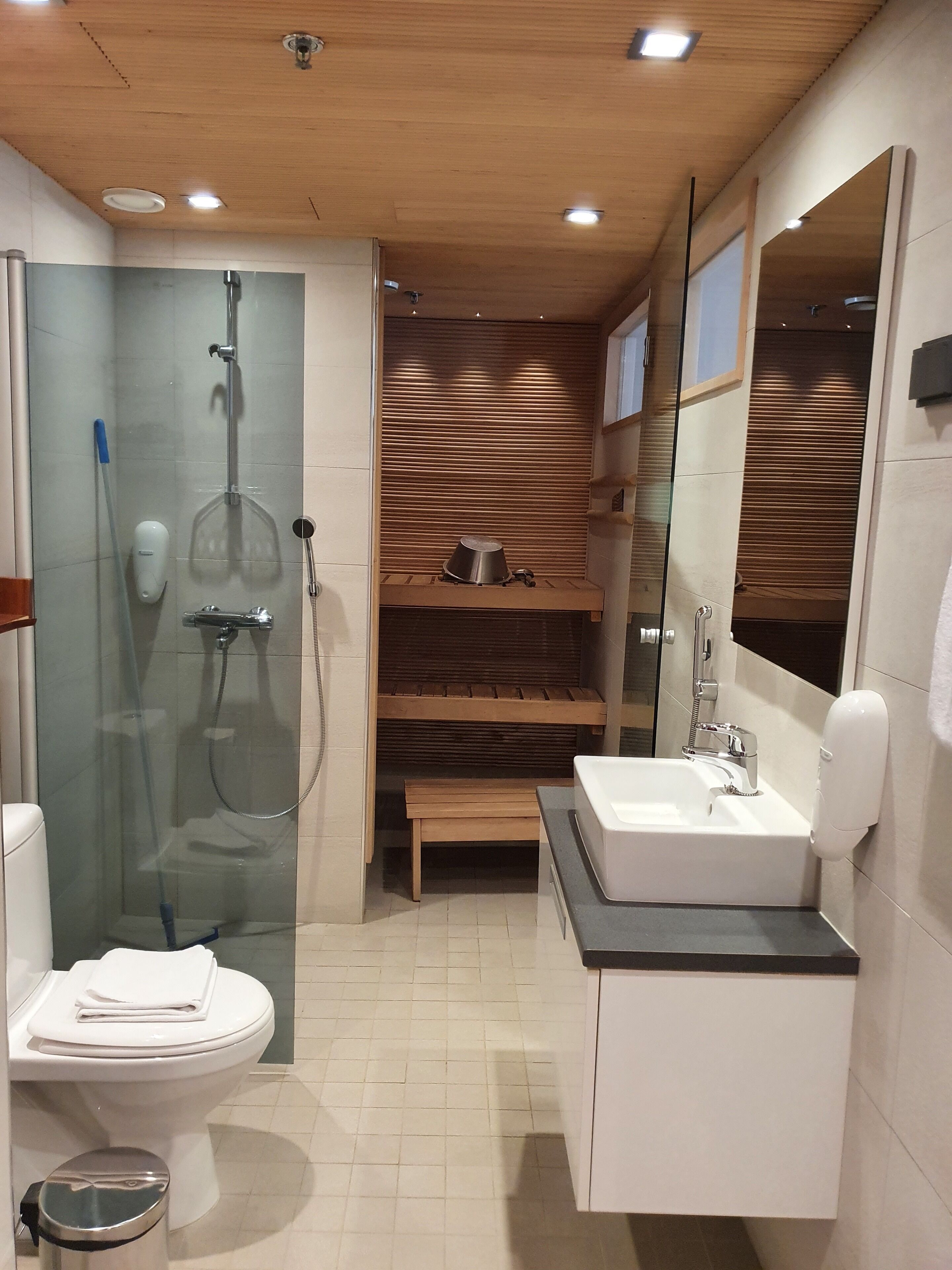 Ein modernes Badezimmer mit einer Duschkabine, einer hölzernen Ablage, einem Waschbecken mit Spiegel und einer Toilette.