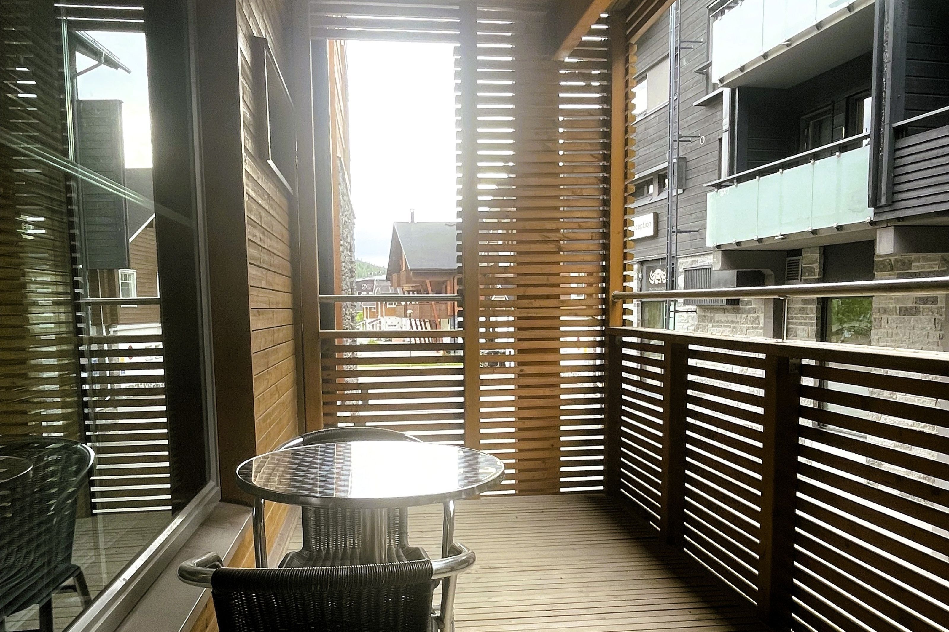 A balcony with a table and chairs, wooden slats, and a view of buildings.
