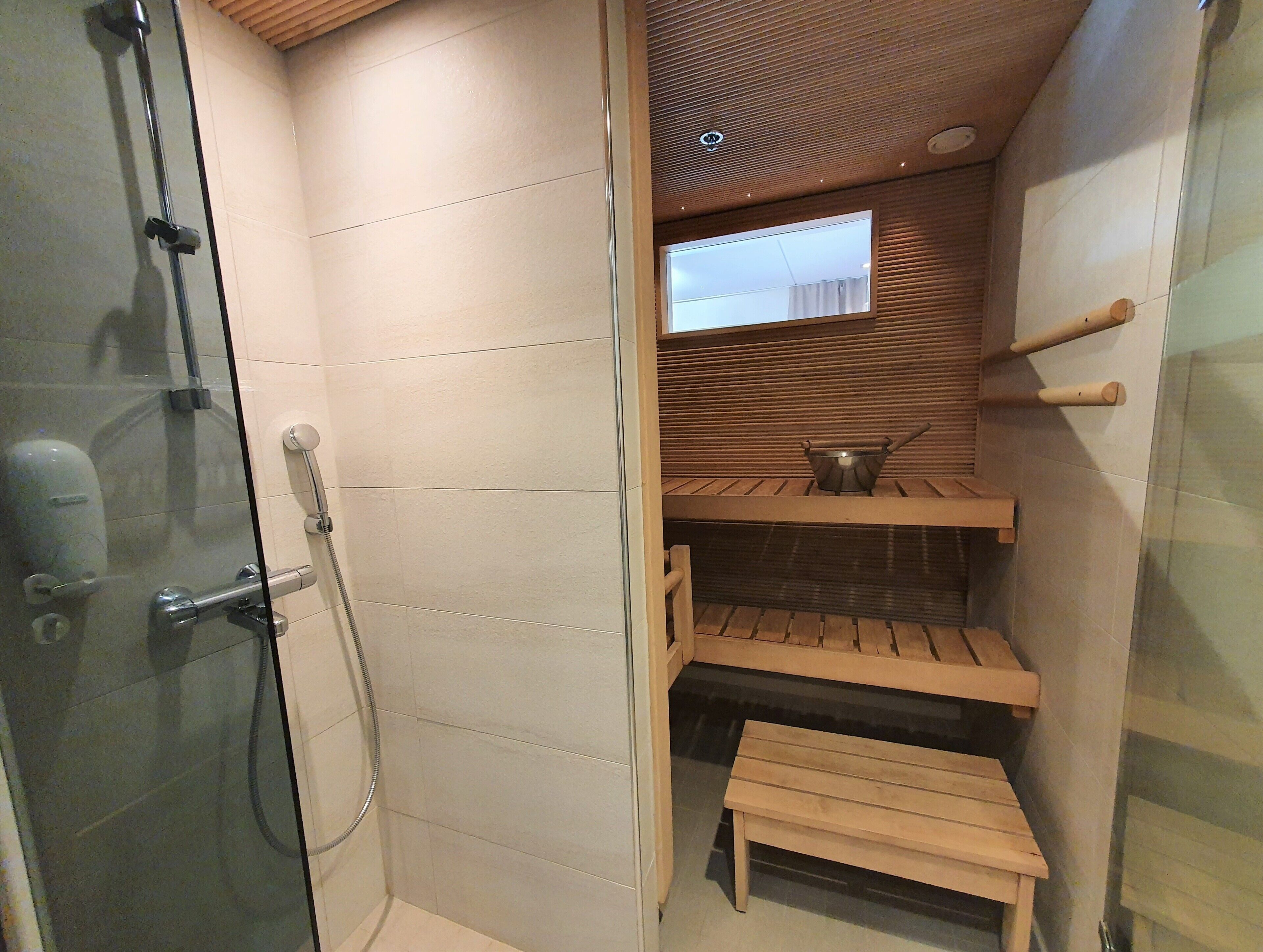A shower area with a glass door, a wooden bench, and a small table with a metal container.