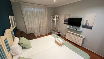 A bedroom with a bed, a TV, a radiator, and a window with curtains.