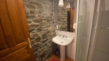 Et badeværelse med stenvæg, hvid vask, spejl og brusebad.