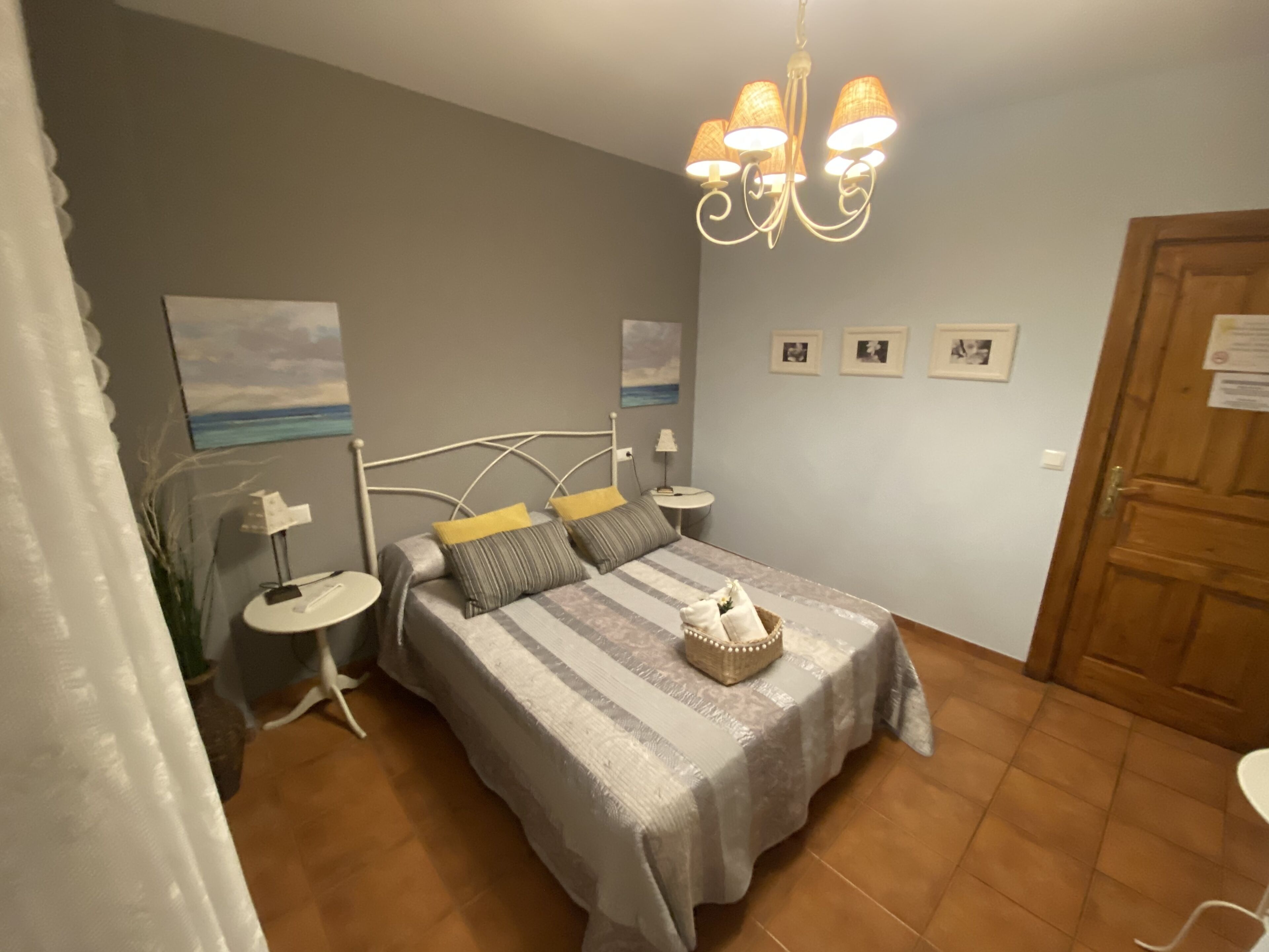 Une chambre à coucher avec un lit, des tables de chevet, un lustre, une porte et un mur décoré de tableaux.