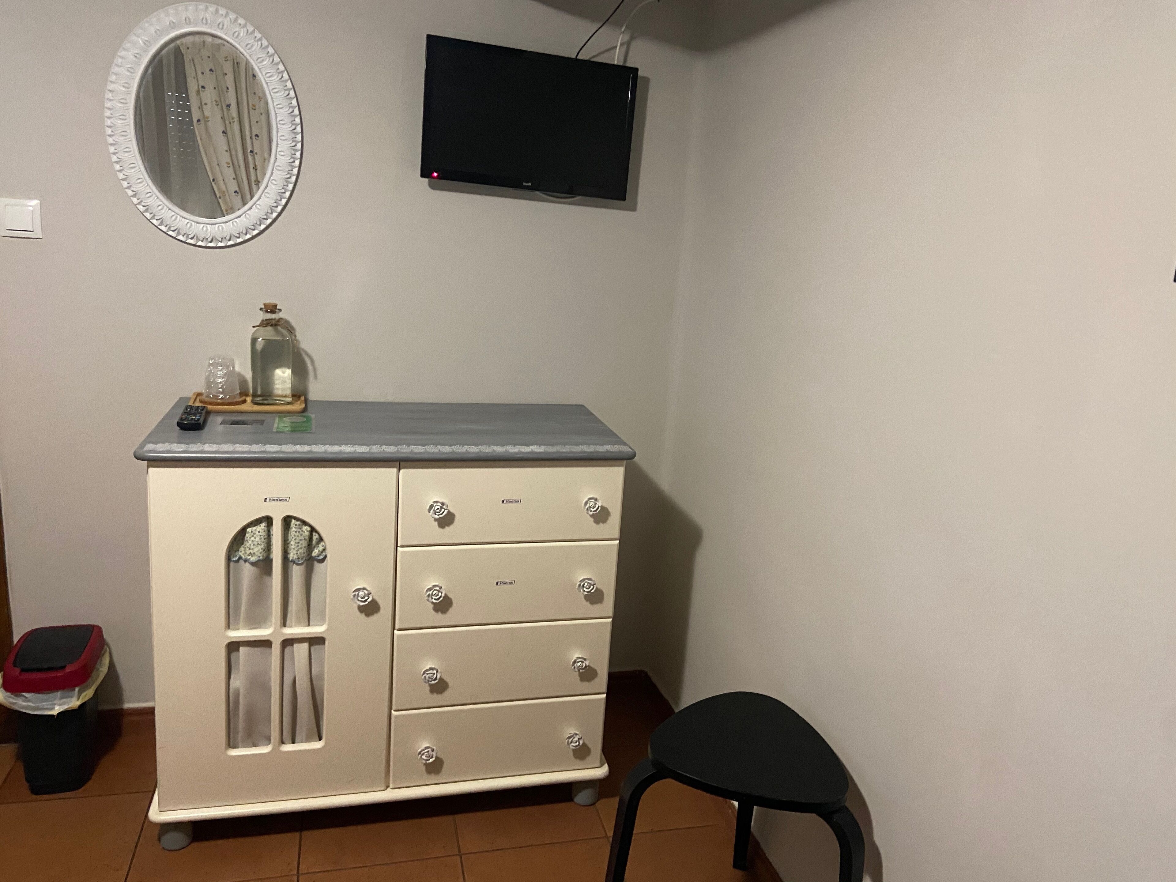A small room with a white dresser, a mirror, a television, and a black chair.