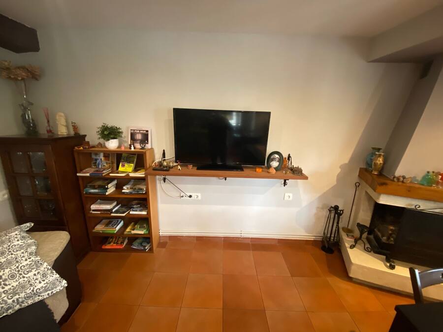 A living room with a flat-screen TV mounted on a wooden shelf, a fireplace, and a bookshelf filled with books.