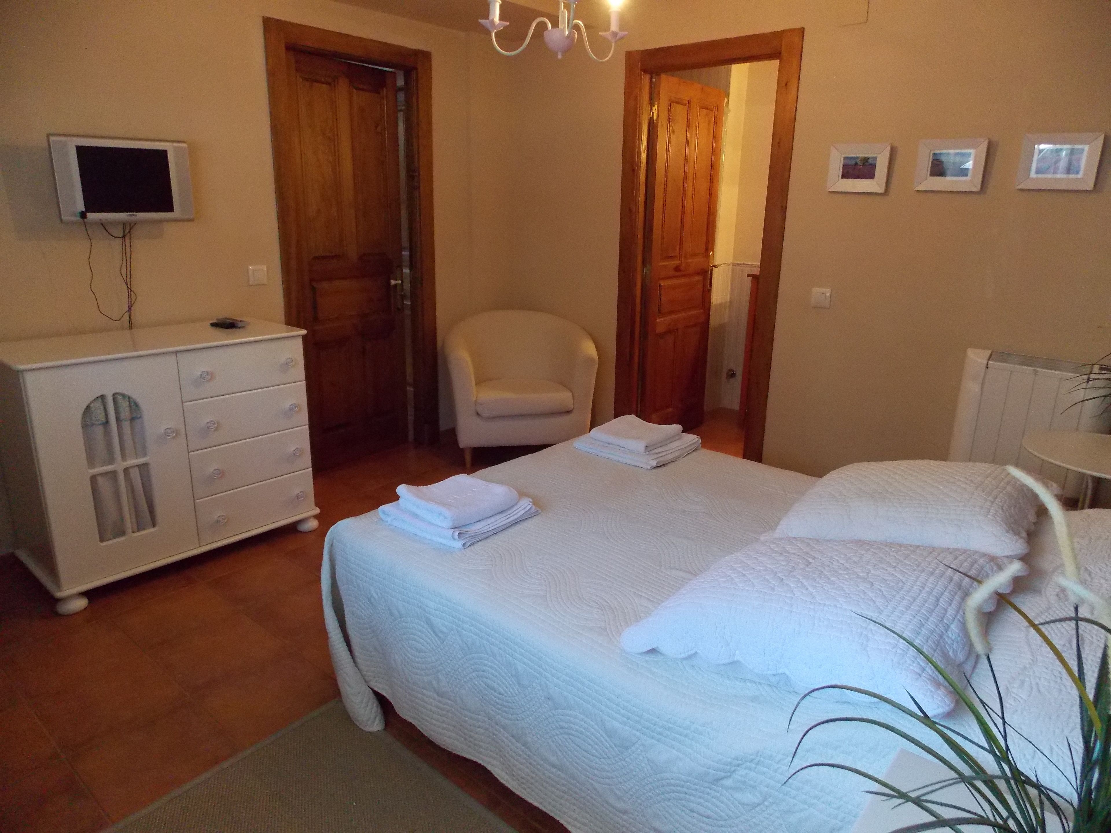 A bedroom with a bed, a chair, a dresser, a TV, and a radiator.